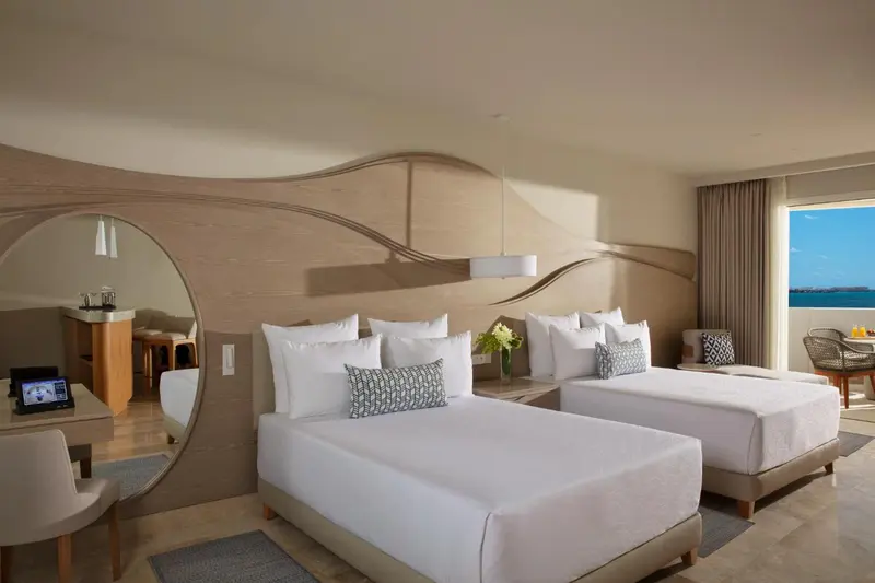 Chambre lumineuse avec deux lits doubles et une vue sur la mer.