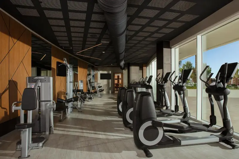 Une salle de sport lumineuse avec des équipements de fitness alignés devant de grandes baies vitrées.