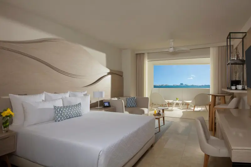 Une chambre lumineuse avec un grand lit et un coin salon donnant sur une vue mer.
