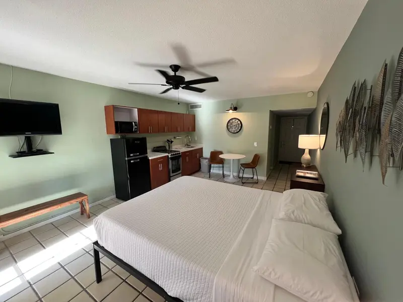 Une chambre lumineuse avec un lit blanc et une kitchenette.