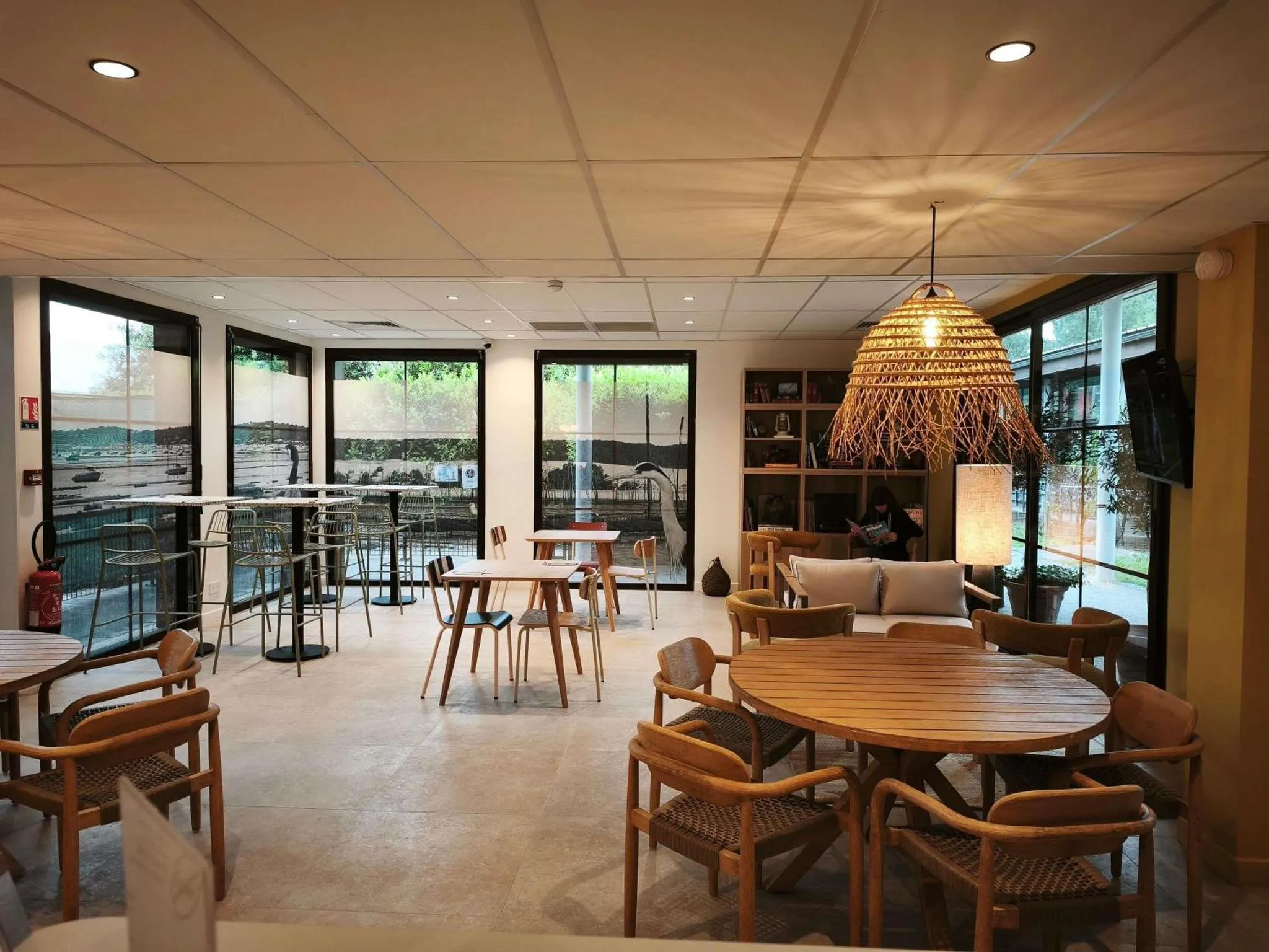 Une salle lumineuse avec des tables et des chaises en bois, éclairée par des suspensions en fibres naturelles.