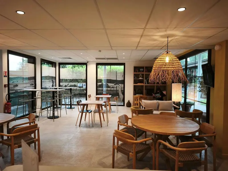 Une salle lumineuse avec des tables et des chaises en bois, éclairée par des suspensions en fibres naturelles.