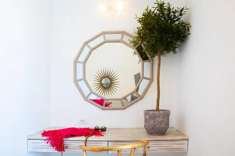 Un miroir octogonal orne un mur blanc au-dessus d'une console en bois clair.