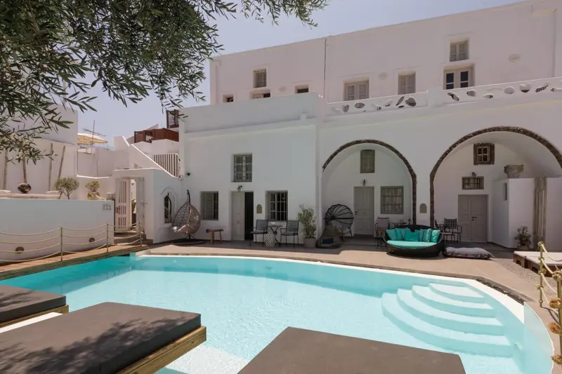 Une piscine turquoise bordée de chaises longues devant un bâtiment blanc aux arches.