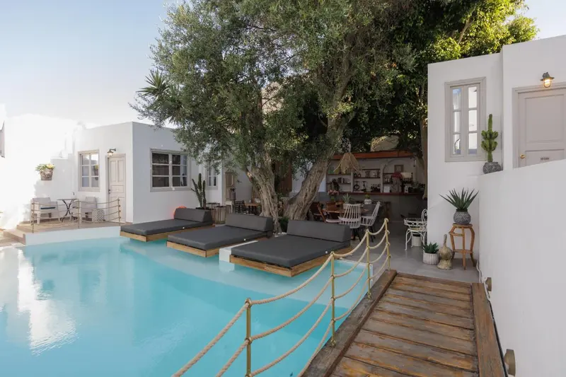 Transats et parasols bordent une piscine turquoise dans une cour ombragée.