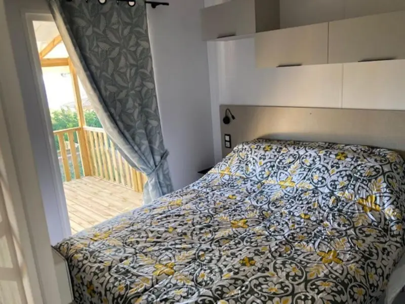 Une chambre avec un lit recouvert d'une couette à motifs et une terrasse en bois visible par une ouverture.