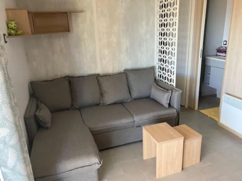 Un canapé d'angle gris et deux petites tables basses en bois clair dans un intérieur lumineux.