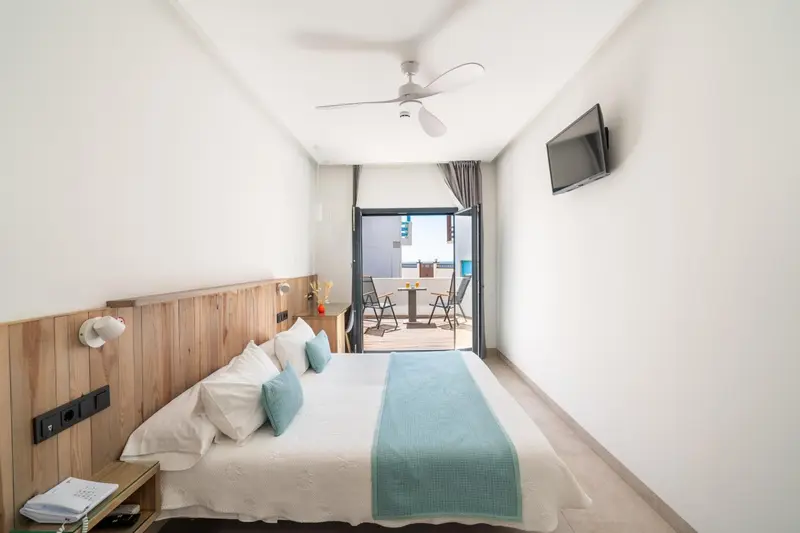 Chambre lumineuse avec un grand lit et une terrasse ensoleillée.