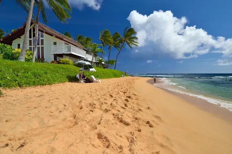 Plage de sable fin bordée de végétation et d'un bâtiment blanc.