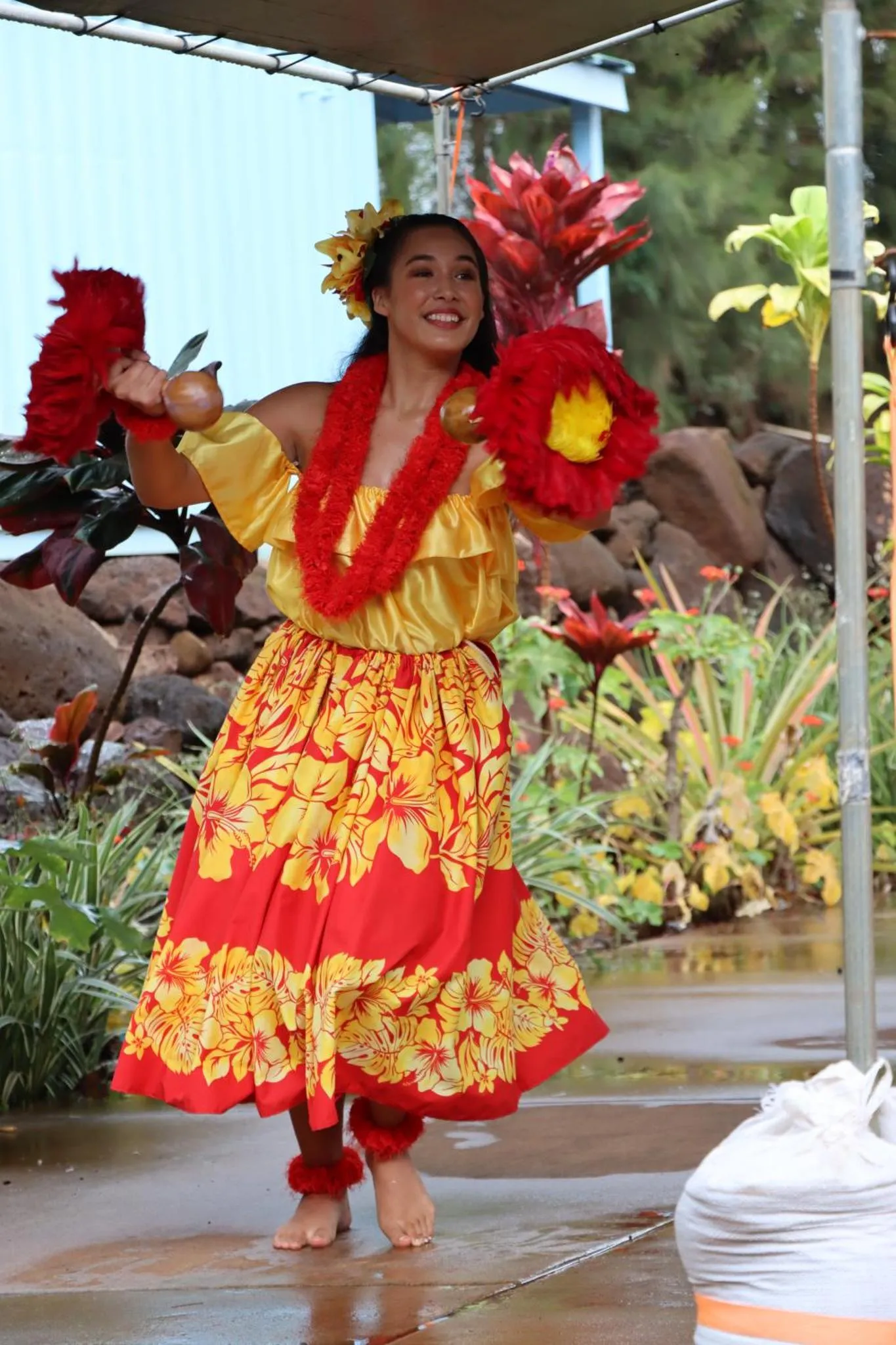 Une jeune femme danse avec des fleurs et des accessoires colorés dans un jardin tropical.