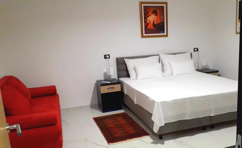 Une chambre lumineuse avec un grand lit et un fauteuil rouge.