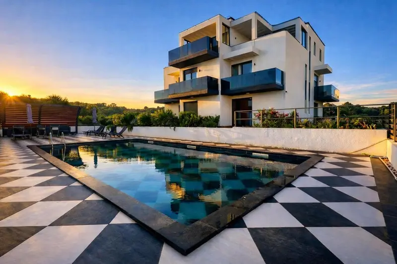 Bâtiment moderne blanc avec des balcons donnant sur une piscine rectangulaire et une terrasse carrelée.