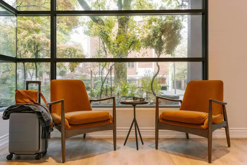 Deux fauteuils orange et une valise attendent dans un espace lumineux.