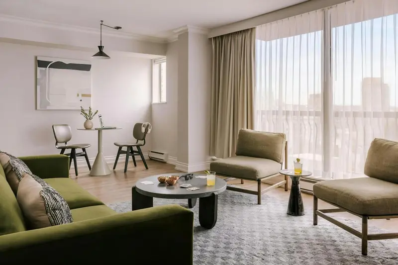 Espace de vie intérieur avec canapés, fauteuils et table basse près d'une grande fenêtre.