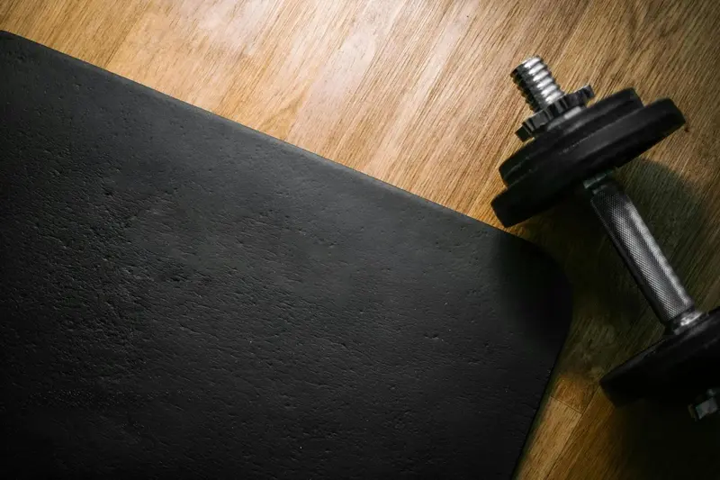 Un tapis de sol noir et un haltère reposent sur un plancher en bois clair.