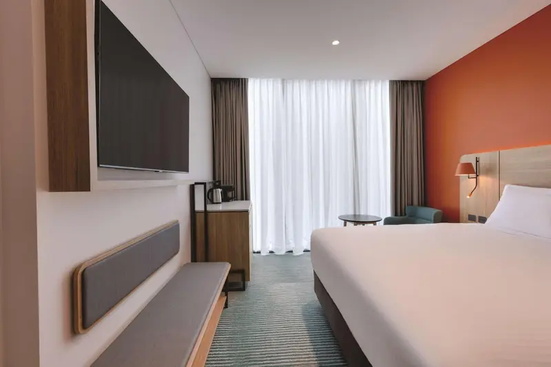 Chambre moderne avec un grand lit et une télévision murale.