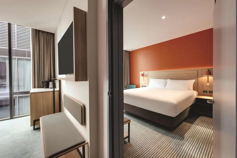 Une chambre d'hôtel moderne avec un lit blanc et un mur orange.