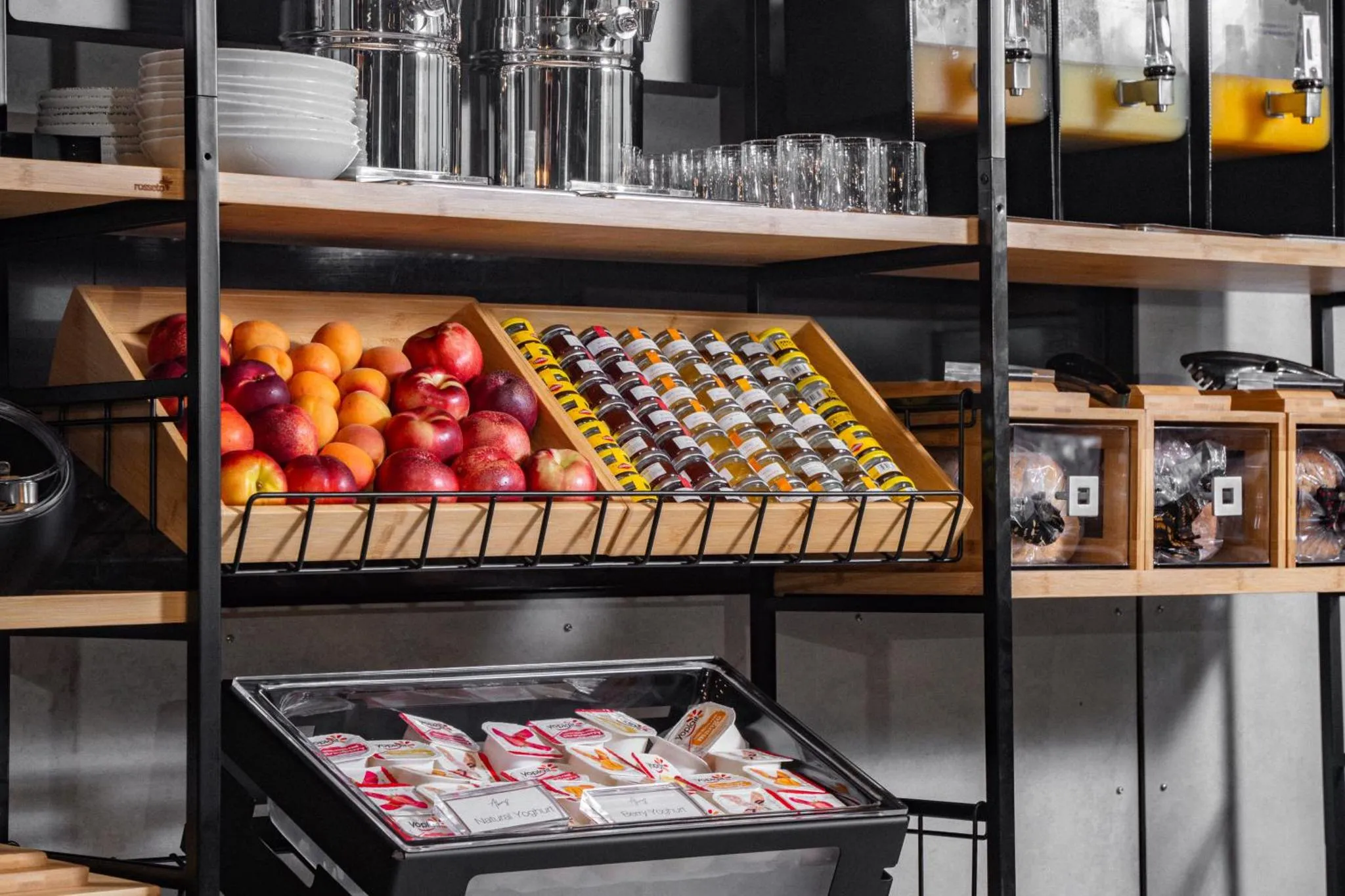 Présentation de fruits, viennoiseries et confitures sur des étagères en bois.