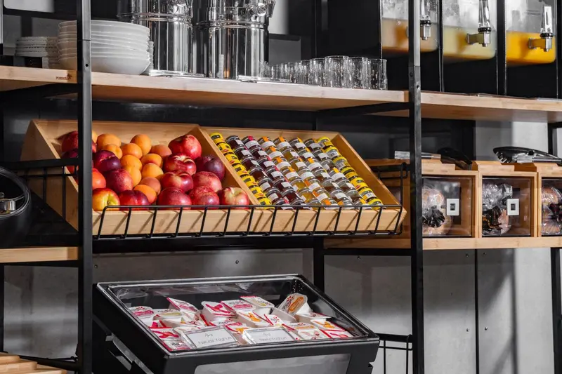 Présentation de fruits, viennoiseries et confitures sur des étagères en bois.