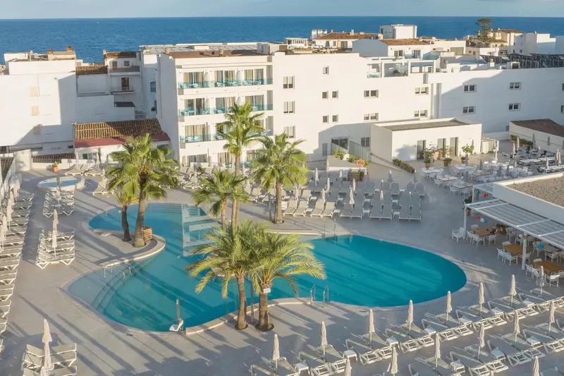 Vue aérienne d'un complexe hôtelier blanc avec piscine et palmiers.