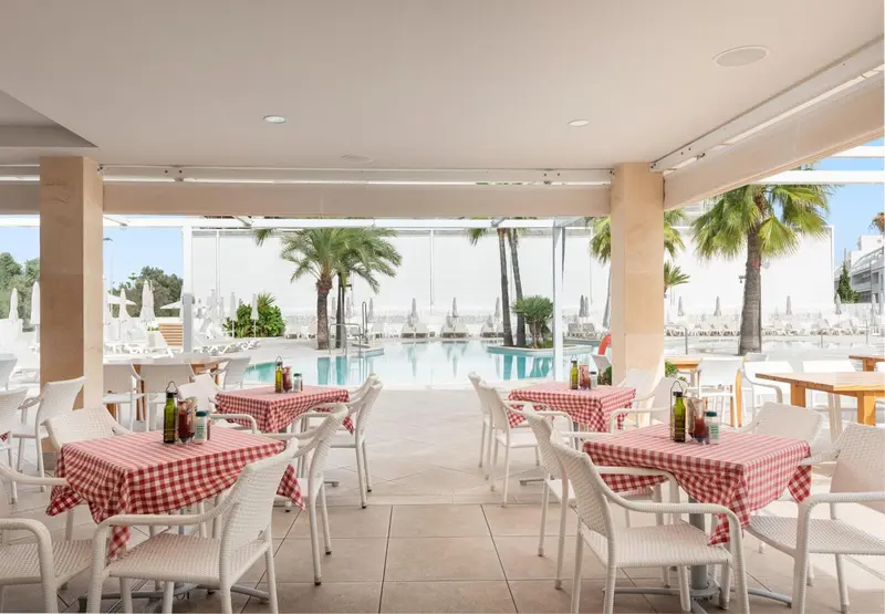 Une salle à manger lumineuse avec des tables nappées en vue sur une piscine et des palmiers.