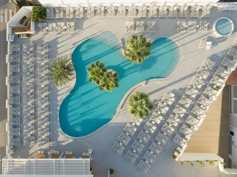 Vue aérienne d'une piscine turquoise entourée de transats et de palmiers.