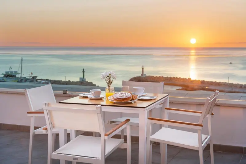 Une table est dressée sur une terrasse avec vue sur la mer au coucher du soleil.