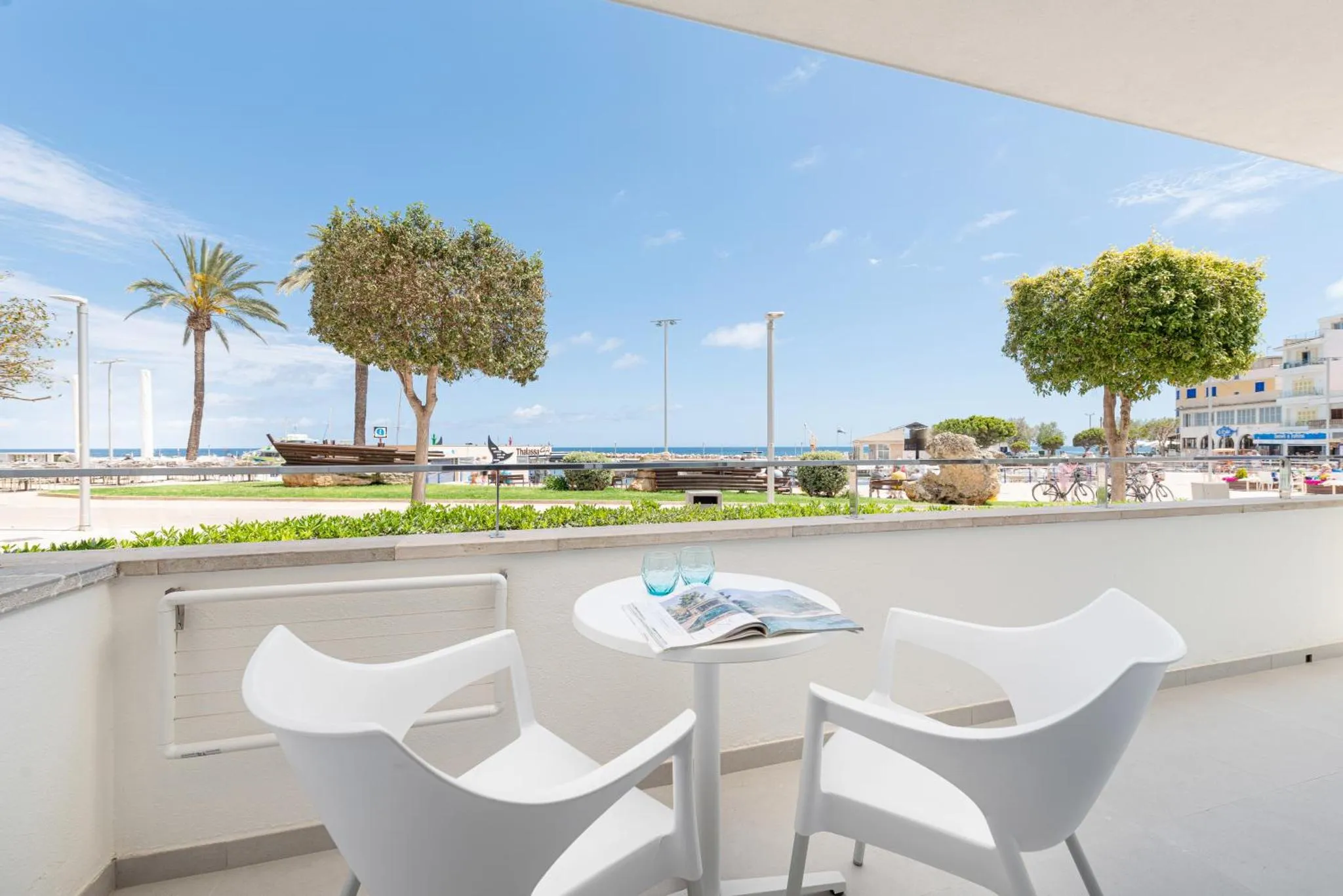 Une table et deux chaises blanches sur une terrasse ensoleillée avec vue sur la mer et la promenade.