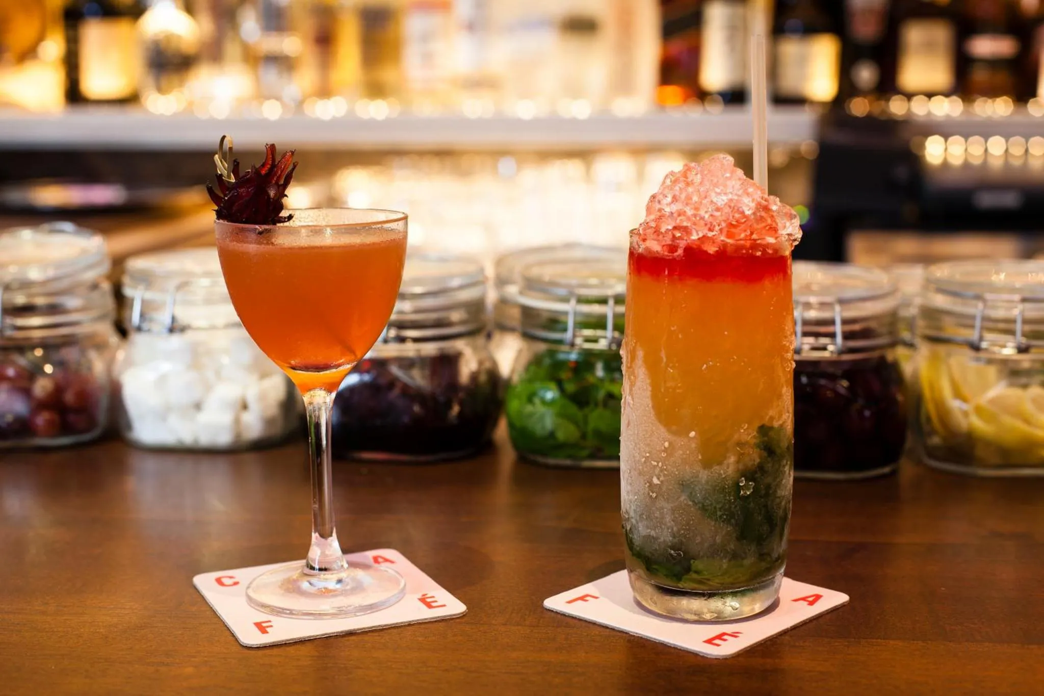 Deux cocktails colorés sont servis sur un comptoir en bois.