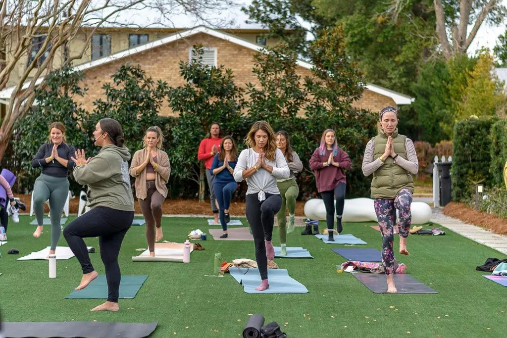 Un groupe de personnes pratique le yoga sur une pelouse verte devant un bâtiment.