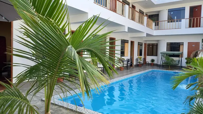 Une piscine turquoise est entourée de palmiers et de chambres d'hôtel.