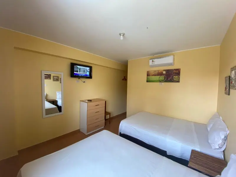 Une chambre lumineuse avec deux lits simples et un téléviseur mural.