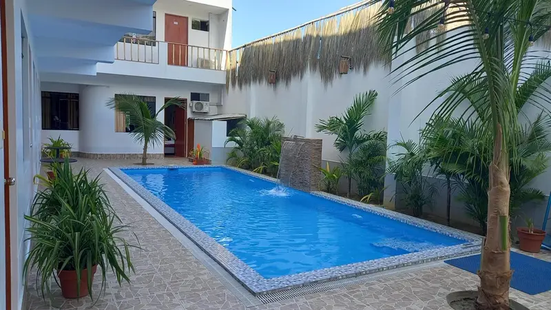 Une piscine rectangulaire entourée de végétation et de palmiers dans une cour intérieure.