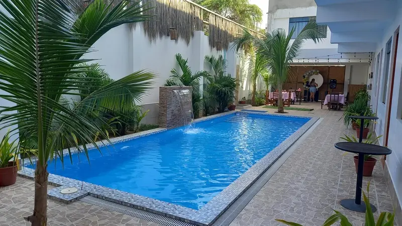 Une piscine rectangulaire entourée d'une terrasse et de végétation tropicale.