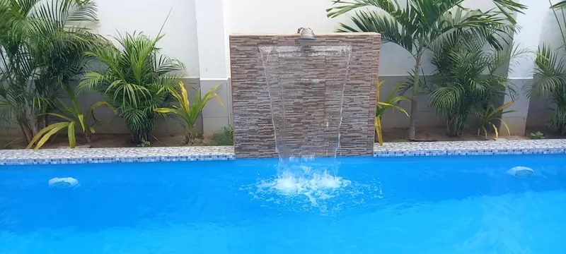 Une piscine rectangulaire avec une cascade artificielle et une végétation tropicale.