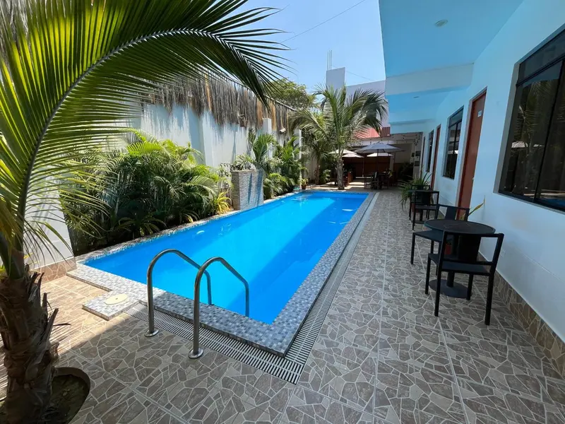 Une piscine rectangulaire entourée d'une terrasse pavée et de végétation tropicale.