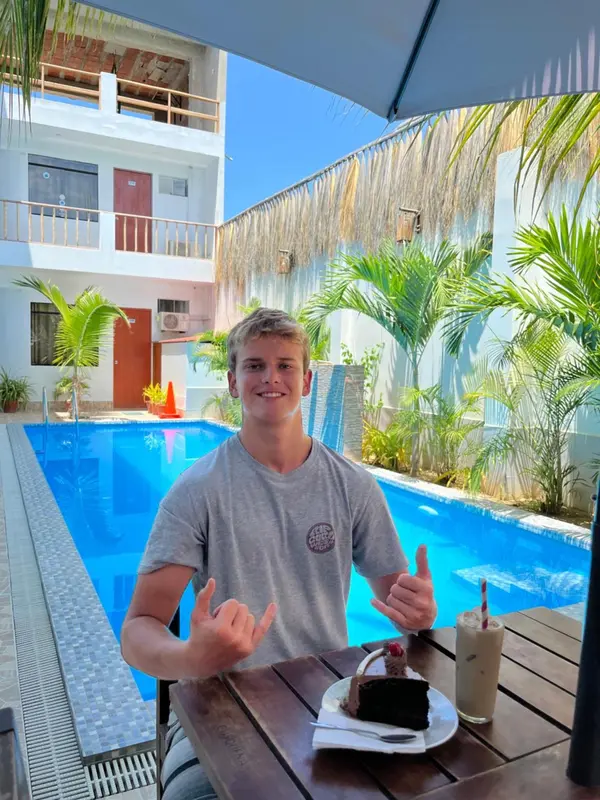 Un homme souriant est assis à une table près d'une piscine avec une boisson et un dessert.