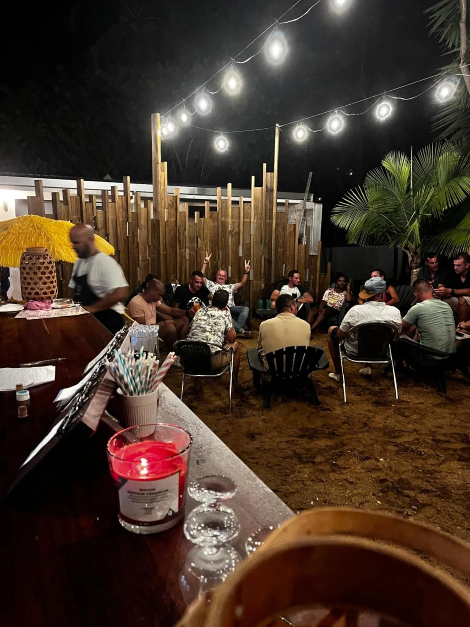 Une terrasse éclairée par des guirlandes lumineuses accueille des clients assis autour de tables basses.