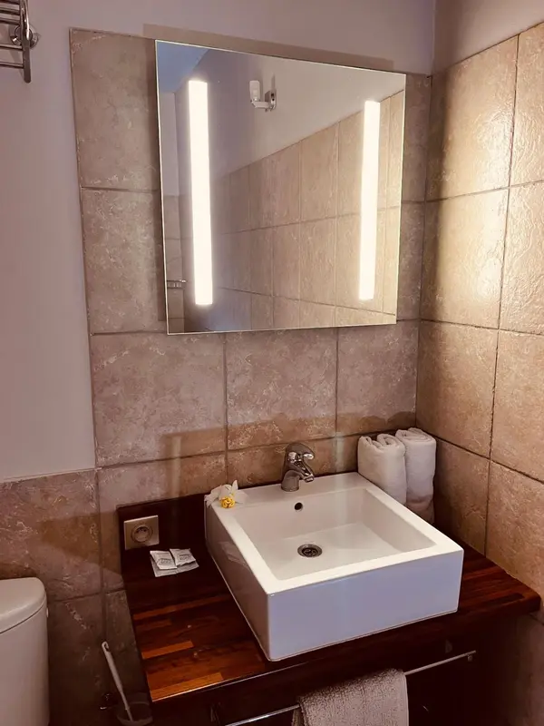Un lavabo blanc et un grand miroir lumineux dans une salle de bain carrelée.