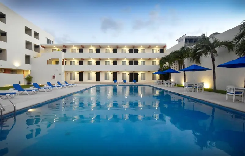 Piscine rectangulaire devant un bâtiment blanc à plusieurs étages.