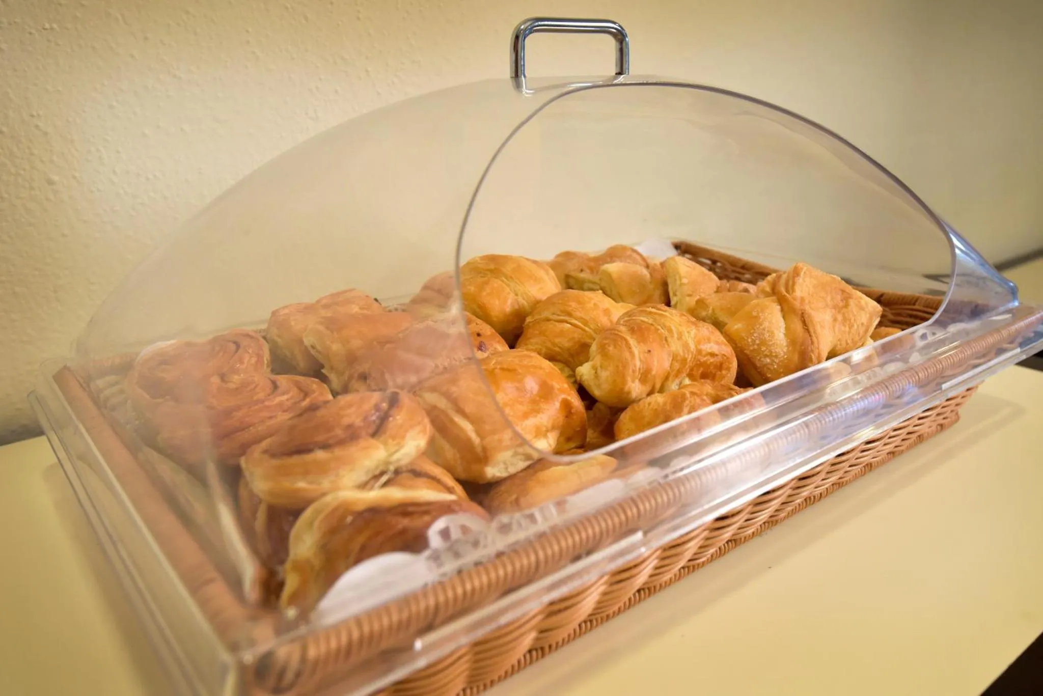 Une corbeille de viennoiseries est présentée sous une cloche transparente.