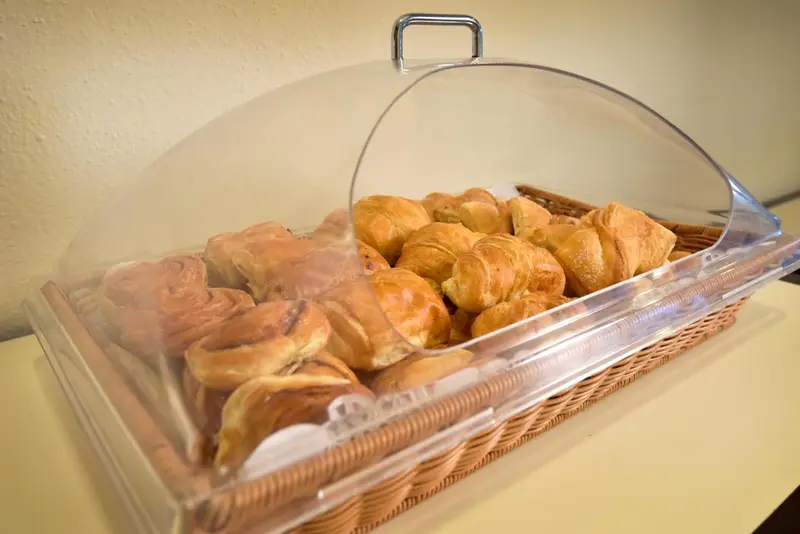 Une corbeille de viennoiseries est présentée sous une cloche transparente.