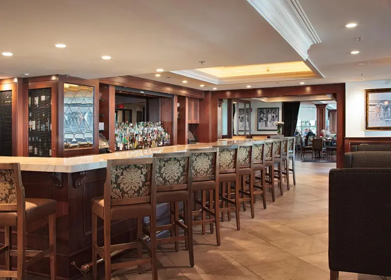 Un long comptoir de bar en bois avec des tabourets est éclairé par des luminaires encastrés.