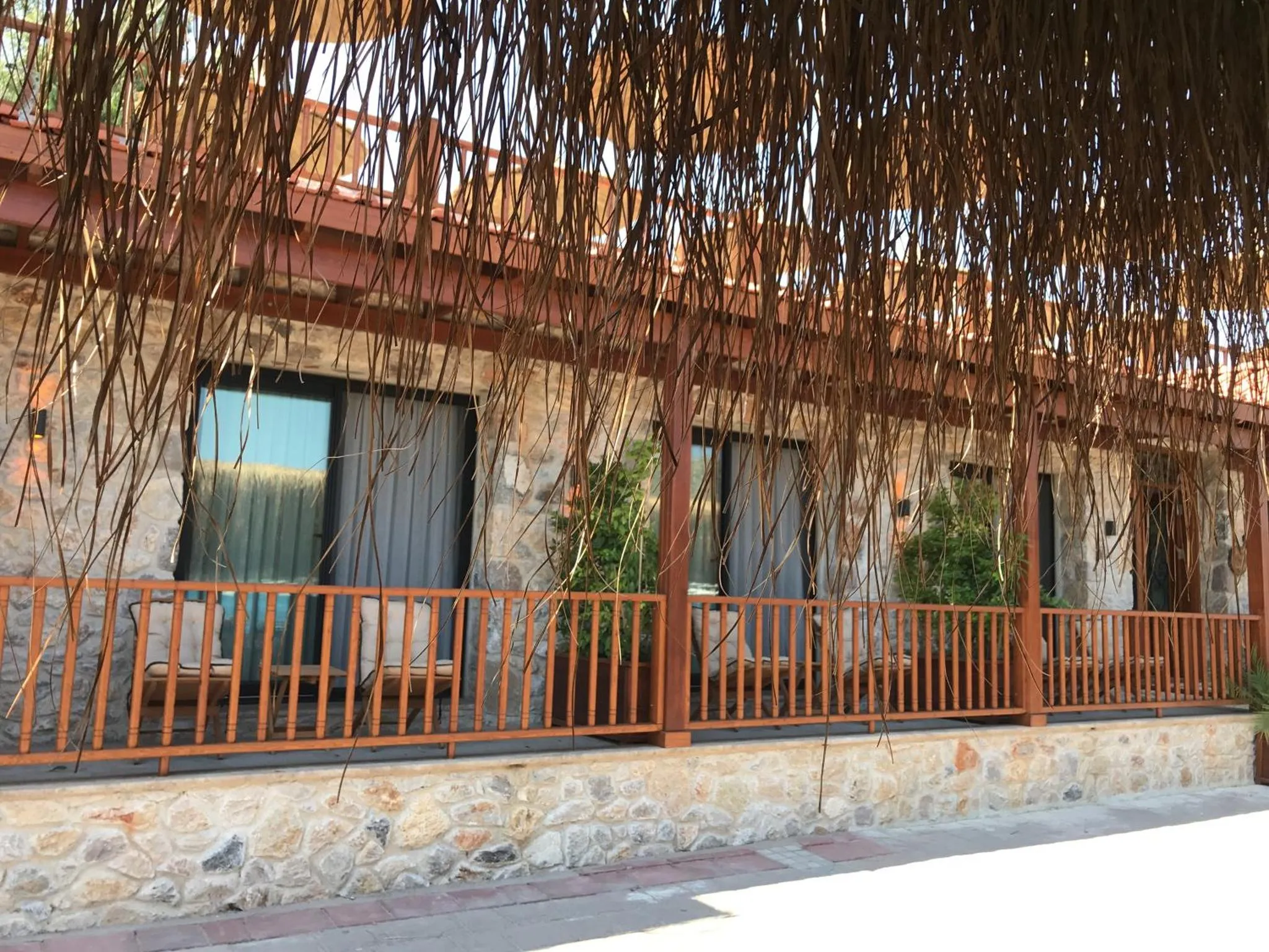 Terrasse ombragée avec des fauteuils en osier devant des murs en pierre.