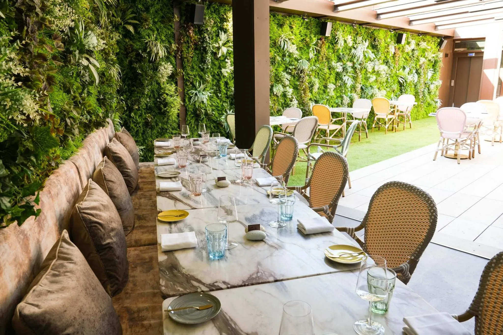 Tables dressées sur une terrasse verdoyante avec des chaises en rotin.