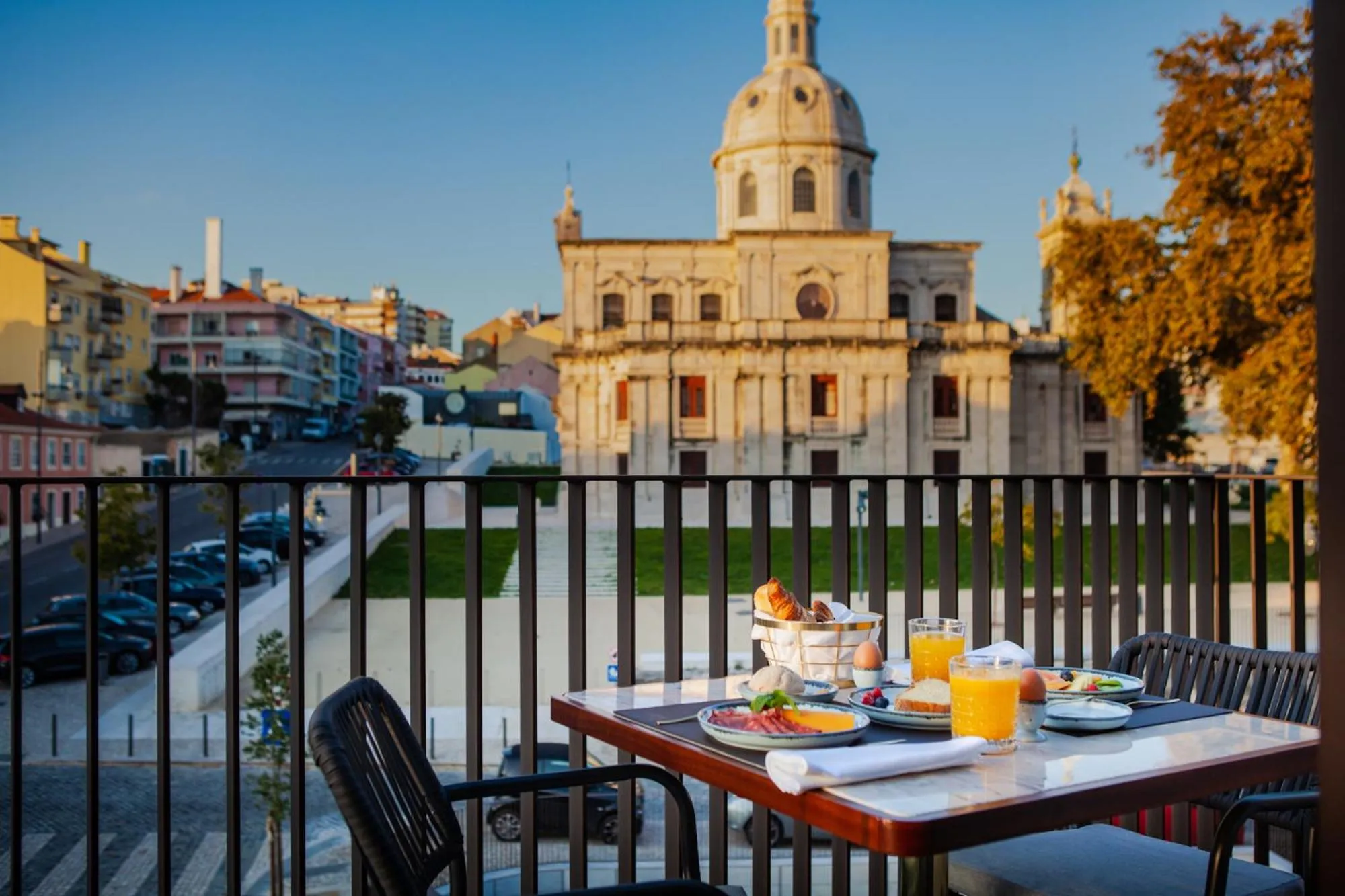 Une table est dressée pour le petit-déjeuner sur une terrasse avec vue sur un bâtiment historique et la ville.