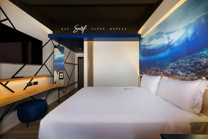 Une chambre lumineuse avec un grand lit et une décoration murale évoquant les vagues.
