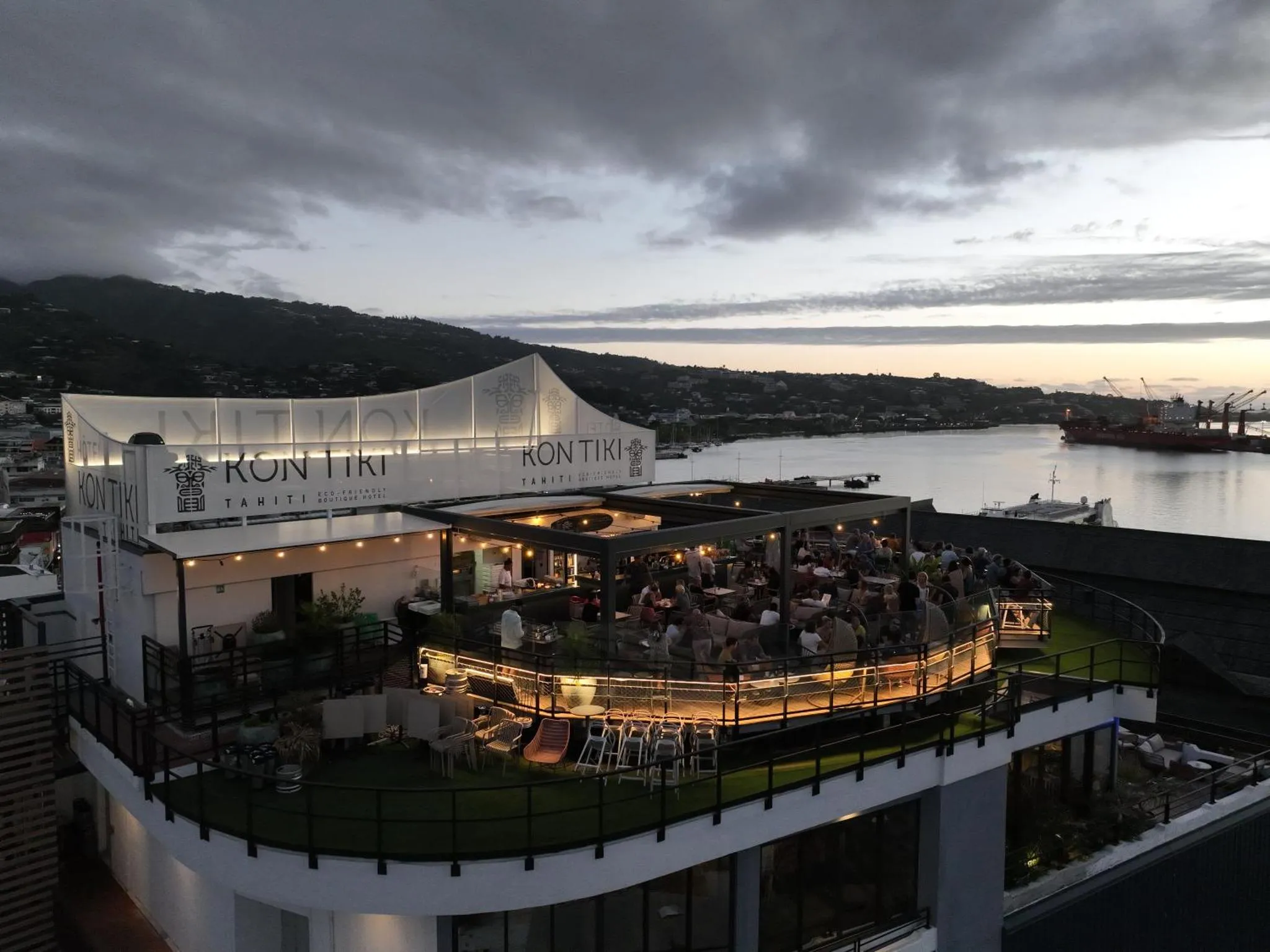 Terrasse panoramique avec tables et chaises, vue sur la mer et la ville.