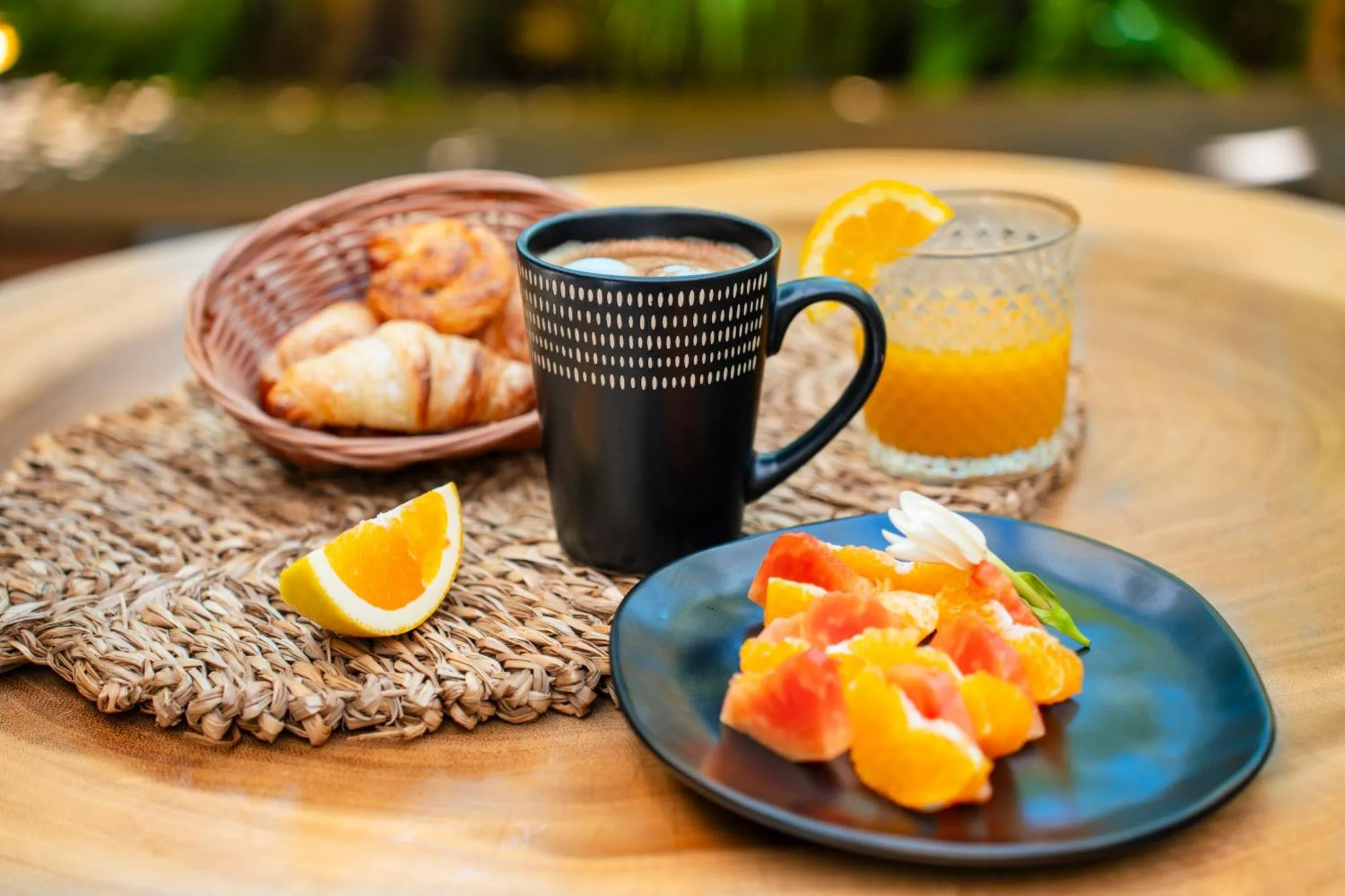 Une table en bois présente un petit-déjeuner avec des viennoiseries, des fruits frais et une boisson chaude.