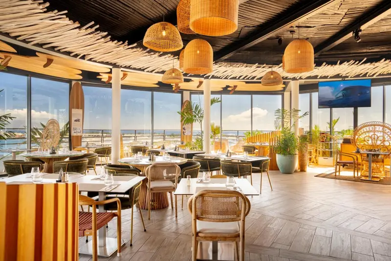 Une salle lumineuse avec des tables dressées et une vue sur la mer.